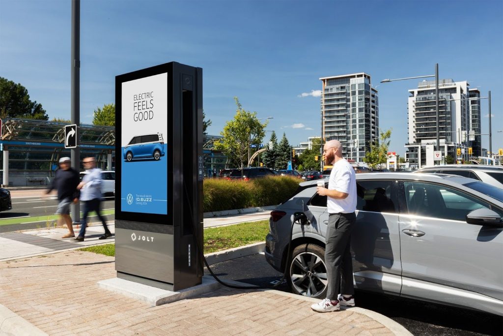 A car charges at a JOLT station, with a DOOH ad being displayed. 